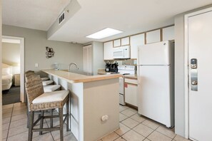 Une cuisine compacte dotée d’un îlot central, de tabourets de bar, d’un four à micro-ondes, d’un réfrigérateur et d’un évier.