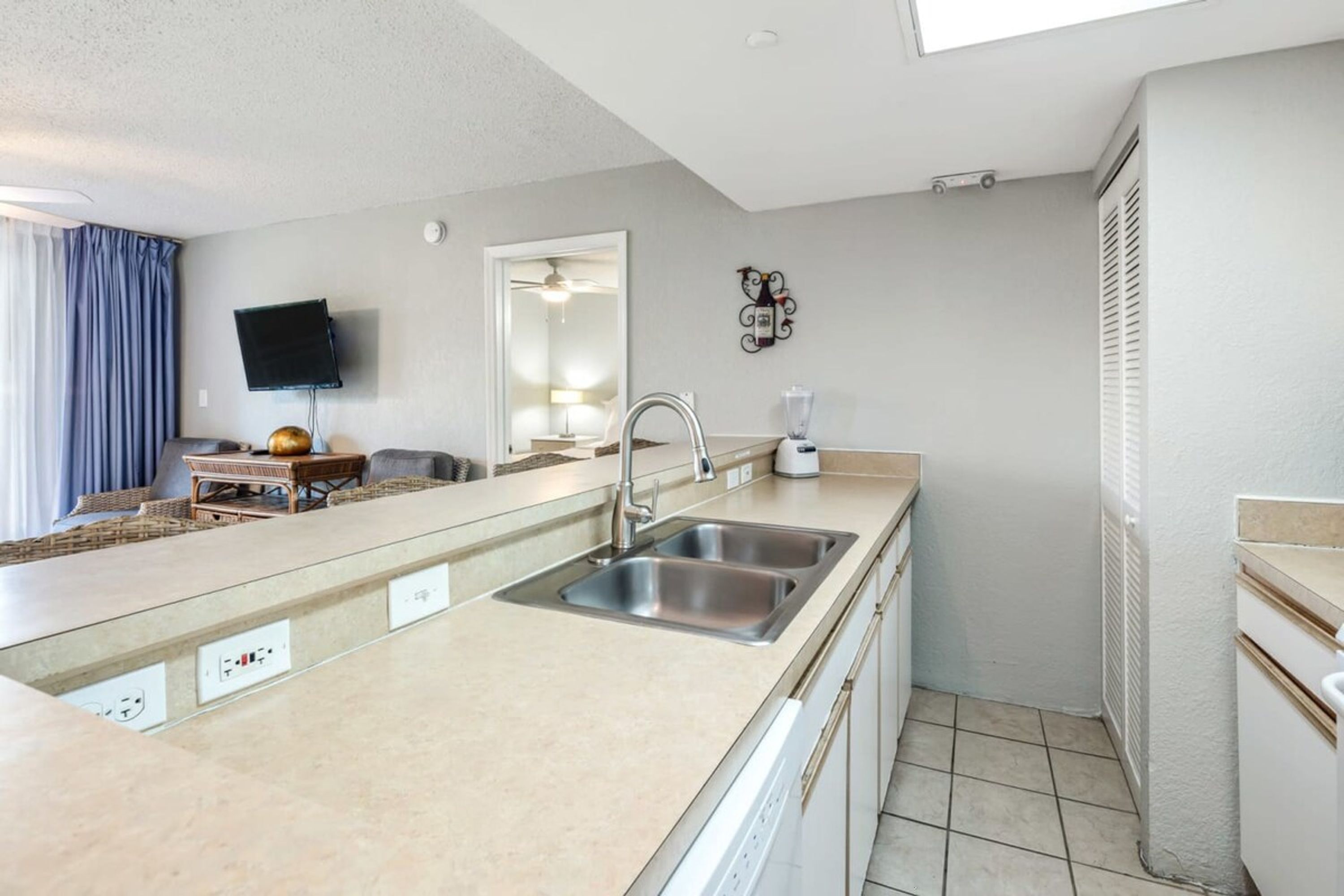 Una cocina compacta con un lavamanos, encimera y un televisor de pantalla plana montado en la pared.