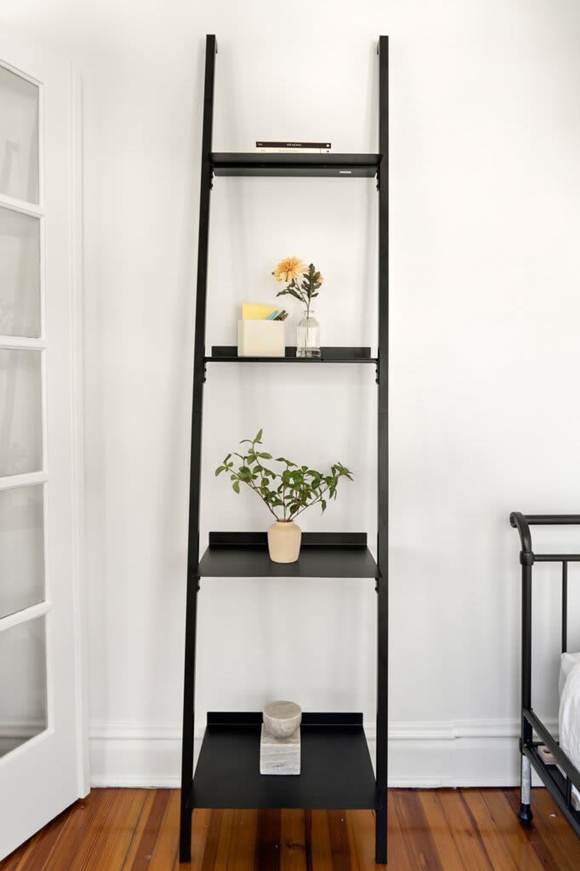A black metal shelf unit with three shelves, each holding a plant and a small decorative item.