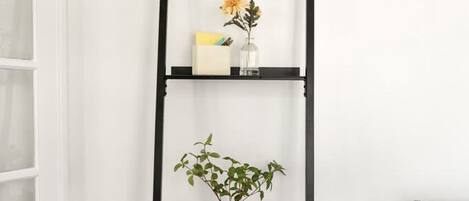 A black metal shelf unit with three shelves, each holding a plant and a small decorative item.
