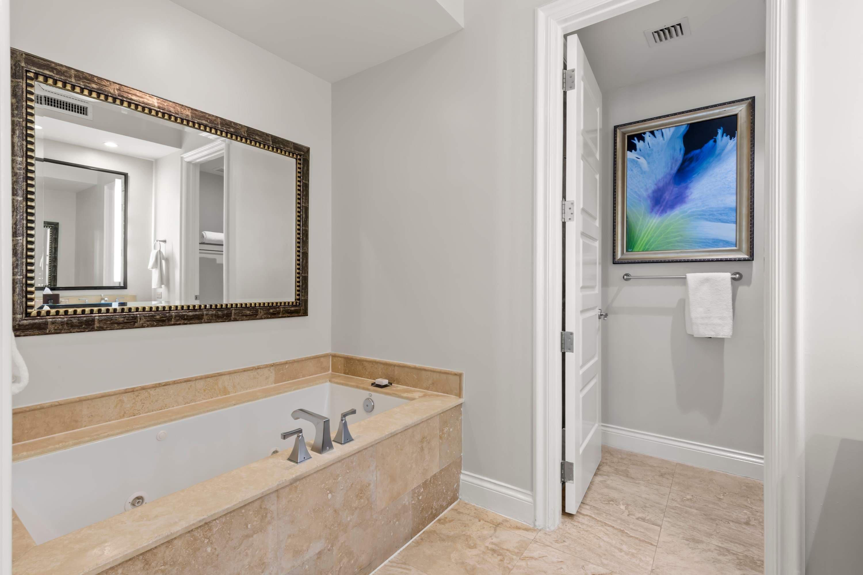 Un bagno con una vasca da bagno ampia, uno specchio con cornice decorativa, un porta asciugamani e un quadro appeso al muro.