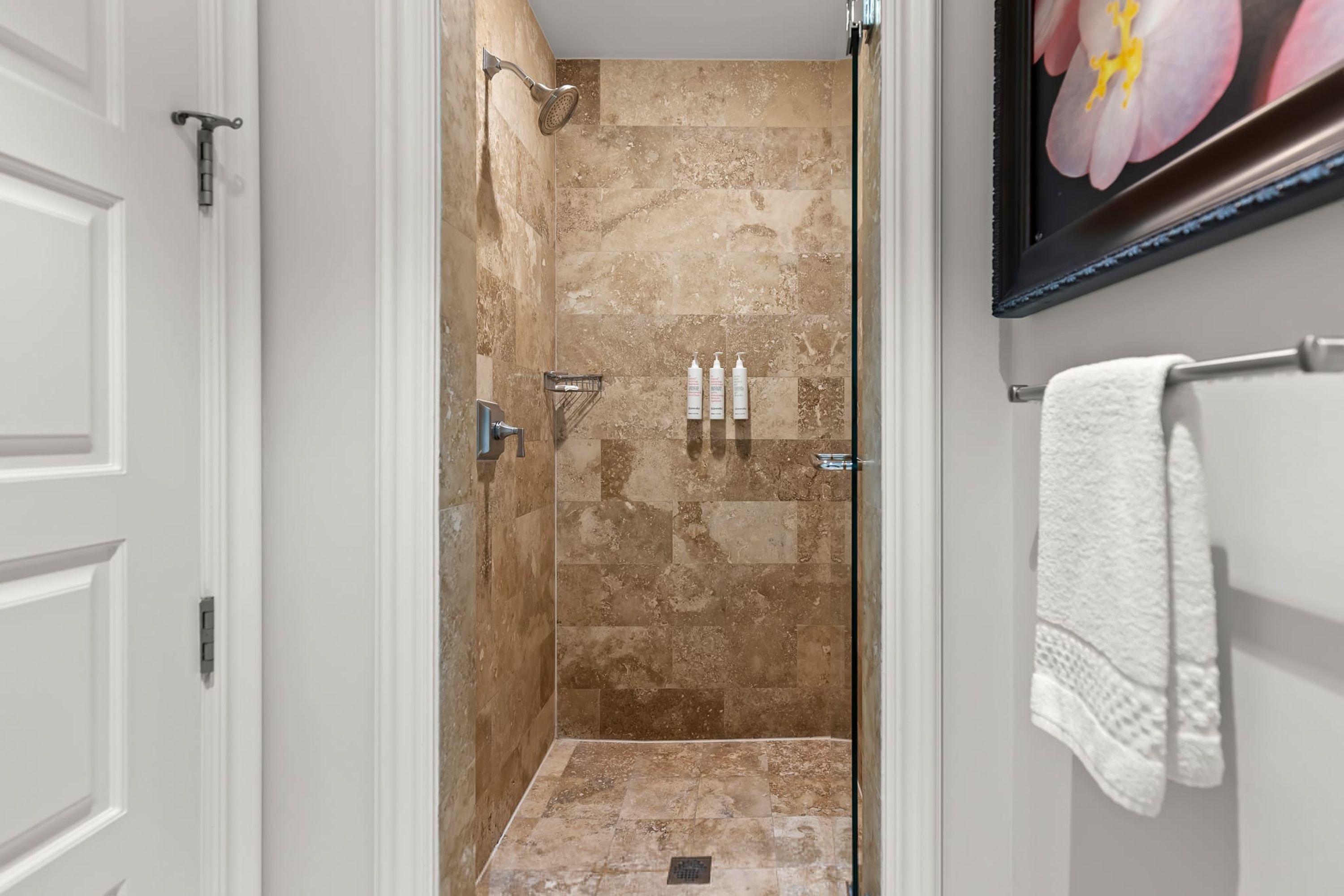 A bathroom with a shower, white tiled walls, a framed picture, and a towel rack.