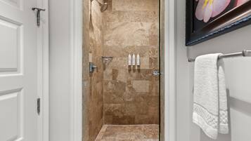 A bathroom with a shower, white tiled walls, a framed picture, and a towel rack.