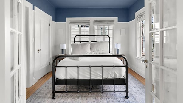 A bedroom with a black metal bed frame, white bedding, and a blue ceiling. - The Adaline 6 Gorgeous Hyde Park Apartment (Tampa)