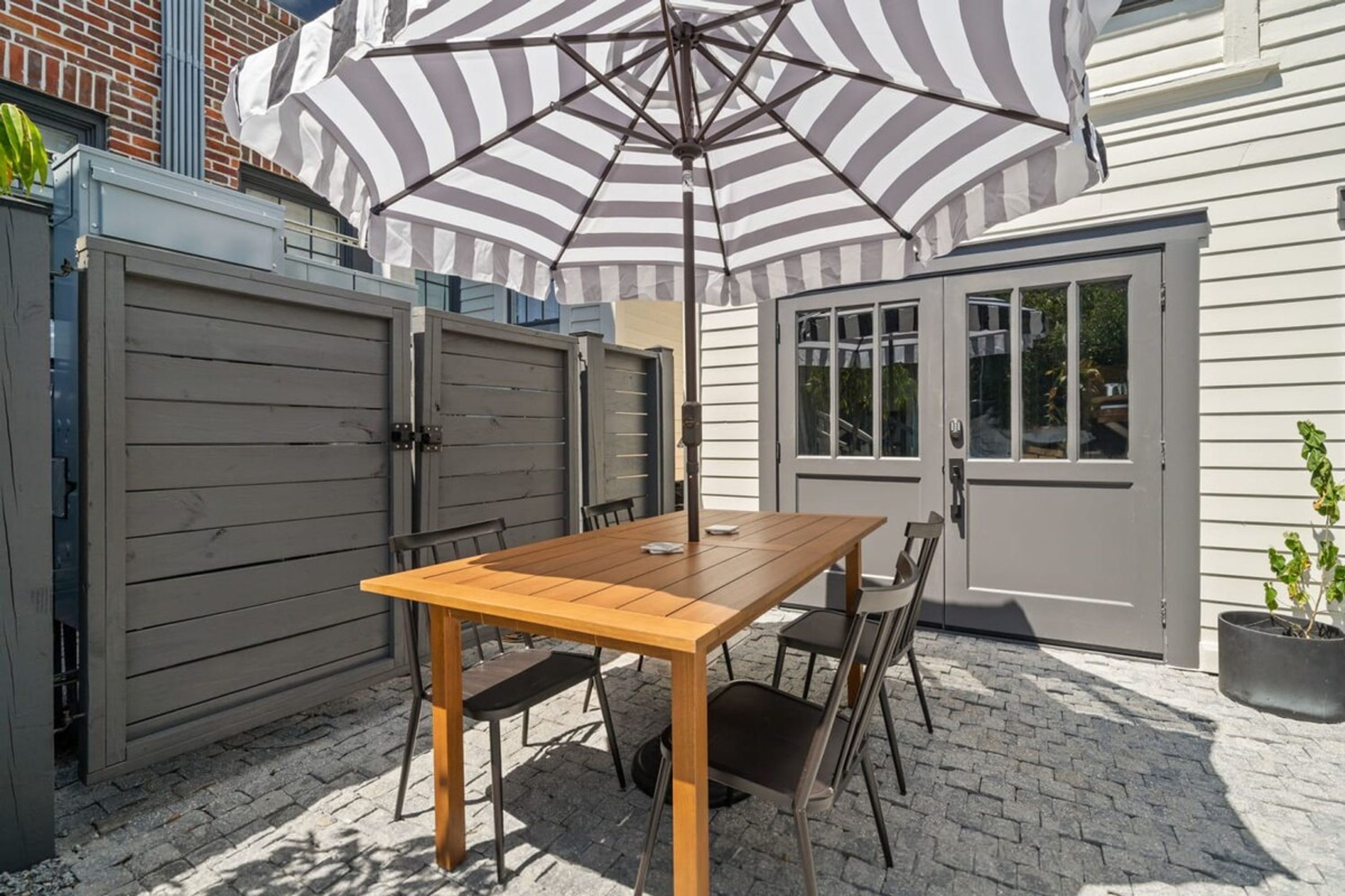 Un patio con mesa y sillas de madera, una sombrilla y una planta en maceta.