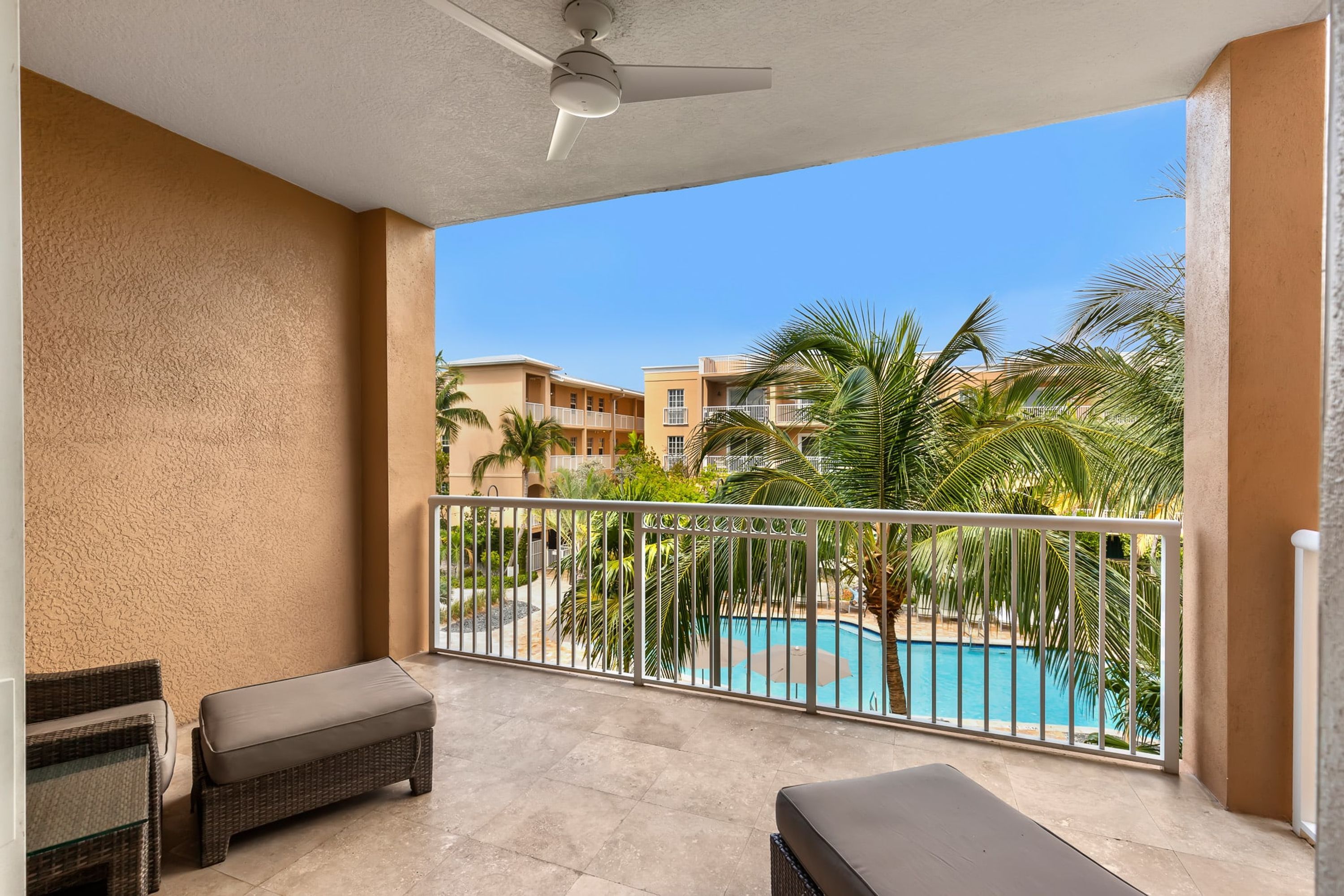 A balcony with a pool view, wicker furniture, and a ceiling fan.
