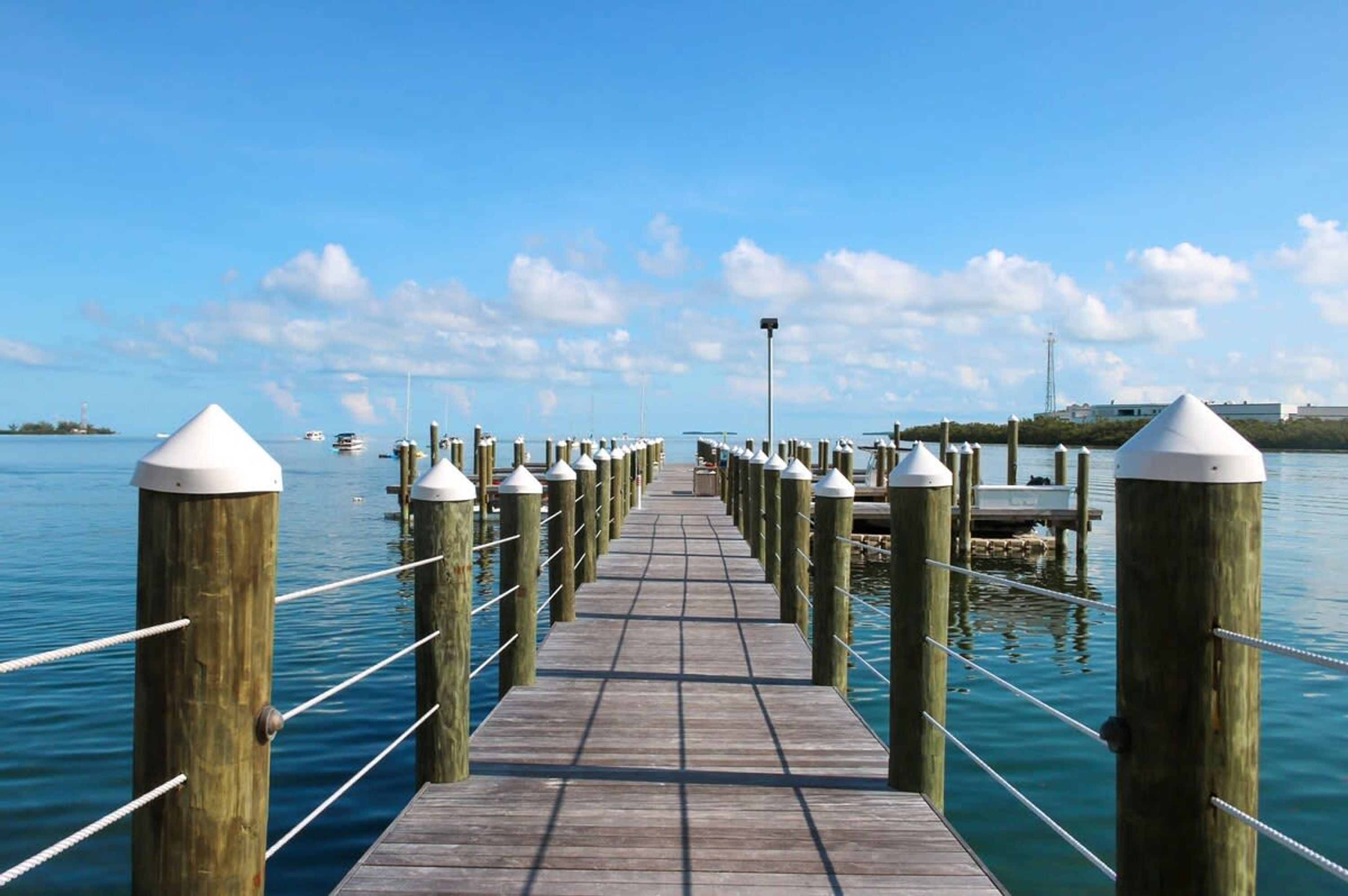 A wooden pier extending into calm water, with evenly spaced bollards and a clear sky.