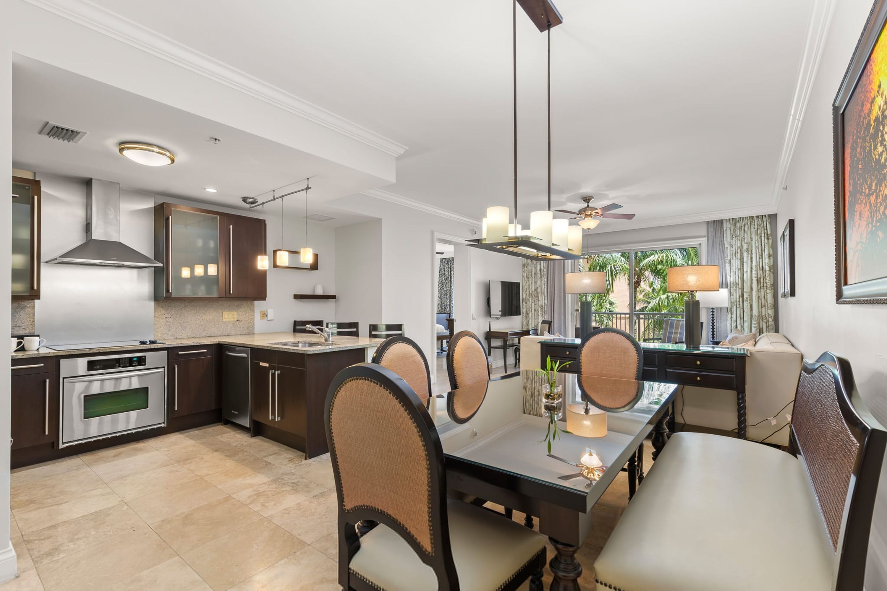 A modern kitchen with dark cabinetry, stainless steel appliances, and a dining area with a glass table and cushioned chairs.