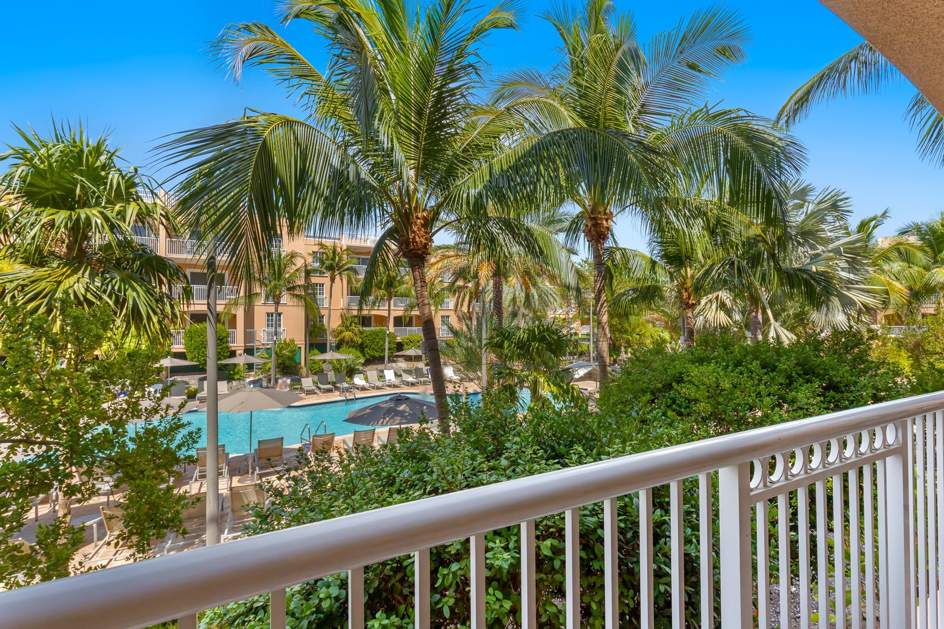 A pool area with lounge chairs and palm trees, surrounded by a building with balconies.