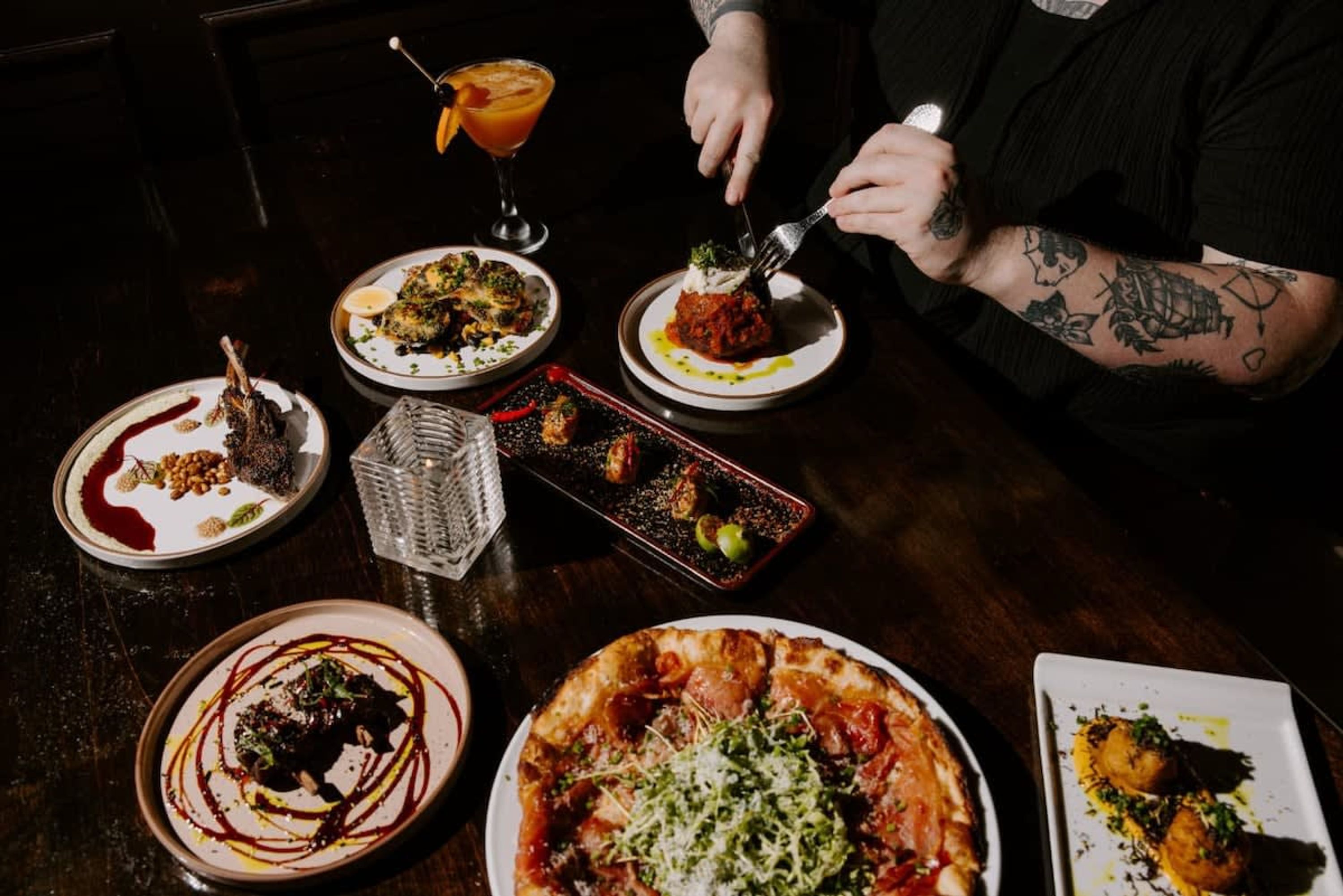 A dining table with various dishes, including a pizza, a dish with a red sauce, and a dessert.