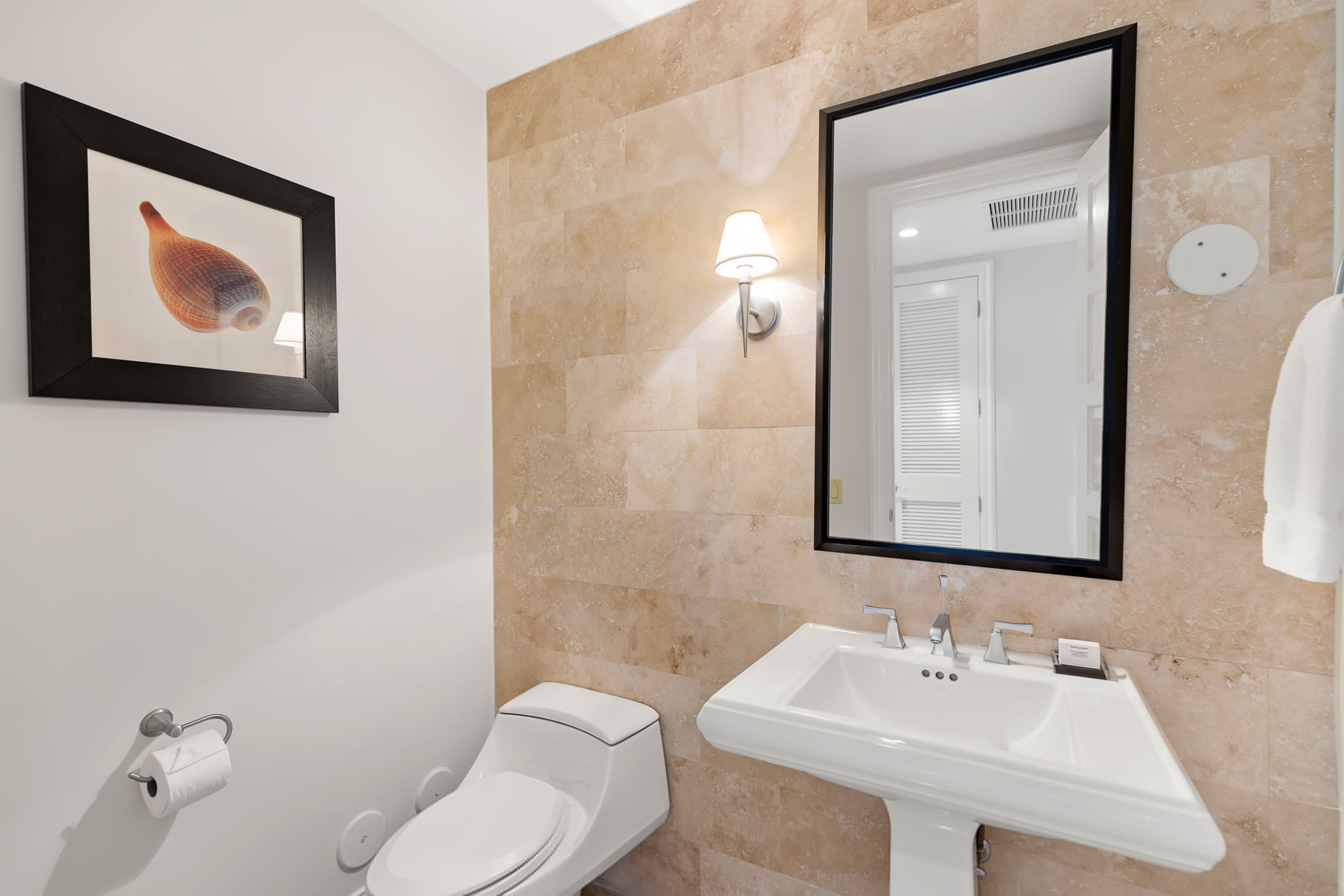 A bathroom with a toilet, sink, and a framed picture on the wall.