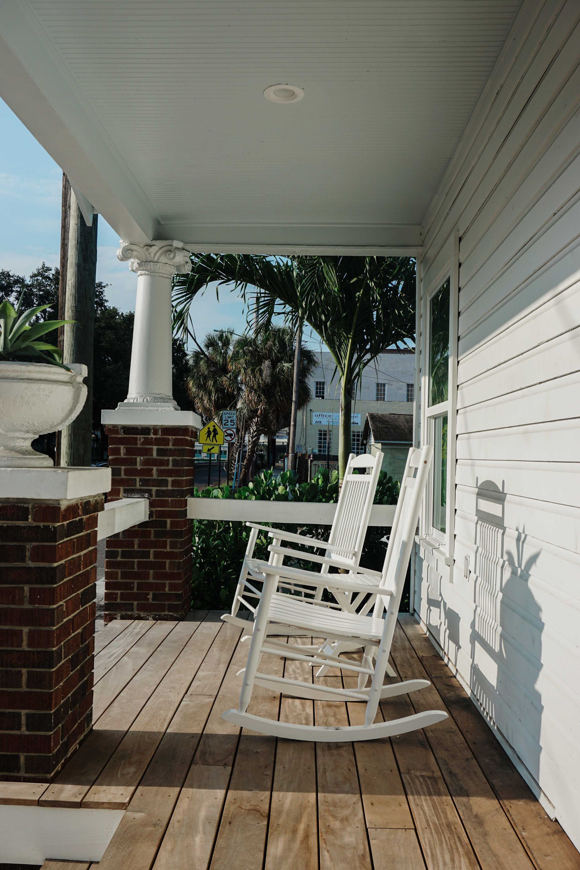 A wooden deck with a rocking chair, a white column, and a brick fireplace.