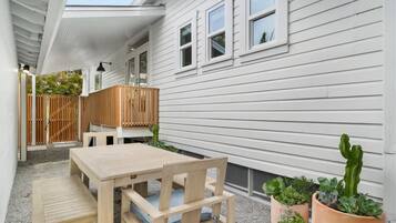 Une table et des chaises en bois sont disposées sur une terrasse en gravier, agrémentée de plantes en pot et d’une clôture en bois.