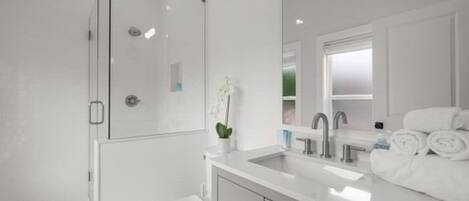 Un baño moderno con cabina de ducha de vidrio, un lavamanos blanco y un espejo sobre el mueble-lavabo.