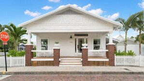 Een wit huis in koloniale stijl met een veranda, bakstenen zuilen en een witte hek.'