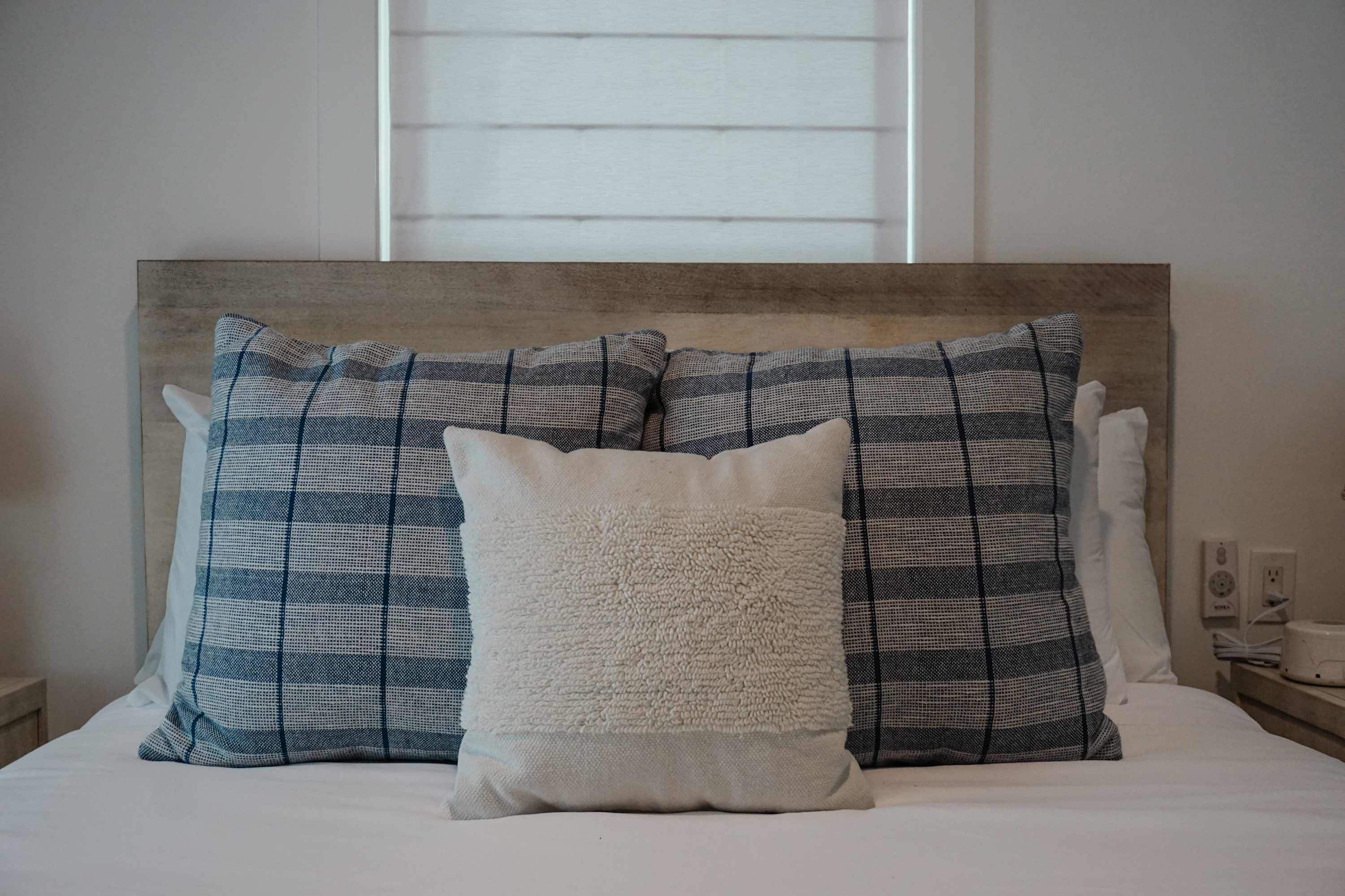 A bed with a headboard, two patterned pillows, and a fluffy pillow.