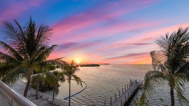 A beach view with palm trees, a wooden pier, and a sunset over the water. - Ocean Front 2BR Residence (Key West)