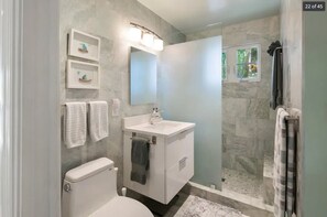 Une salle de bain moderne équipée de toilettes, d’un lavabo et d’une zone douche. Des serviettes sont accrochées au mur et une fenêtre laisse entrer la lumière naturelle.