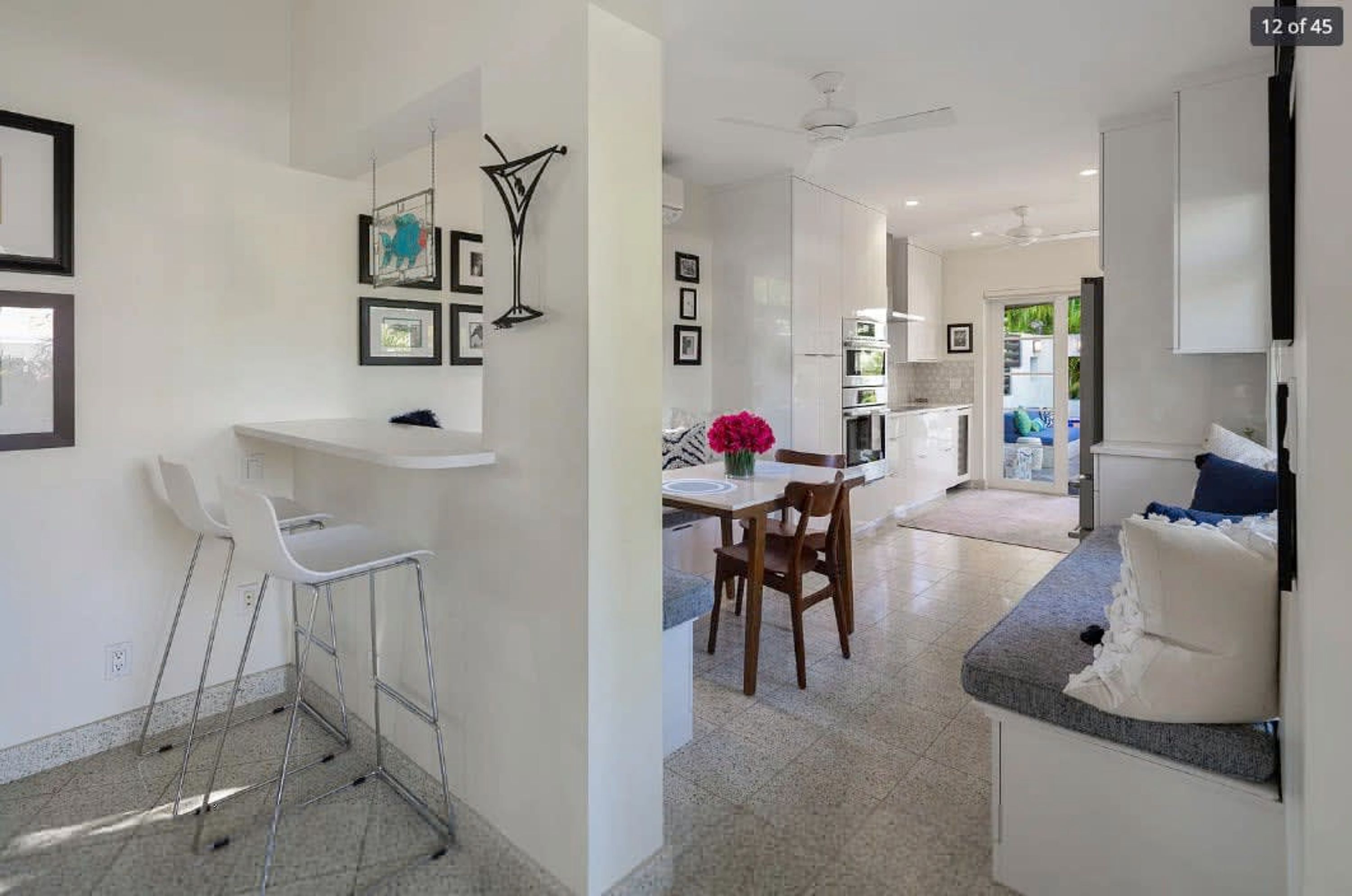 A modern kitchen with white cabinets, a dining area with a table and chairs, and a small seating area with a bench and cushions.