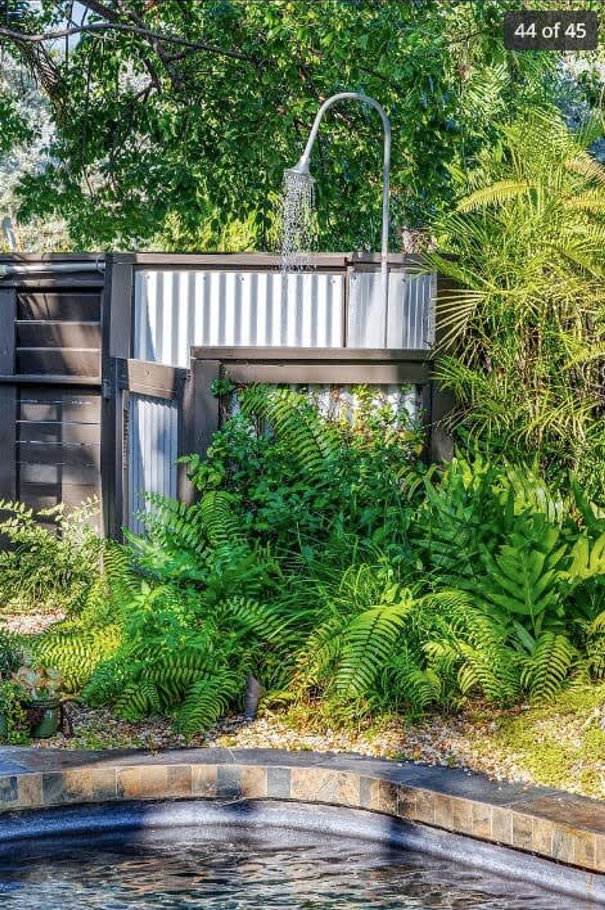 A small outdoor water feature with a fountain, surrounded by lush greenery and a wooden structure.