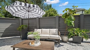 A patio area with a wooden table, a striped umbrella, a beige sofa, and potted plants. - NEW The Adaline 4 Updated Hyde Park Apt (Tampa)
