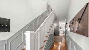 A hallway with a wooden floor, white walls, and a staircase with white railings and wooden steps. - NEW The Adaline 4 Updated Hyde Park Apt (Tampa)