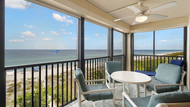 A balcony with a view of the beach, a ceiling fan, and a table with chairs. - Reflections 504 Oceanfront Pool Beach View (Indian Rocks Beach)