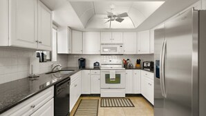 A modern kitchen with white cabinets, stainless steel appliances, and a ceiling fan. - Reflections 504 Oceanfront Pool Beach View (Indian Rocks Beach)