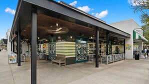 An outdoor seating area with a covered patio, a brick wall with a green and white pattern, and a sign indicating a take-out option. - The Adaline 3 Hyde Park Apt Steps to Bayshore (Tampa)