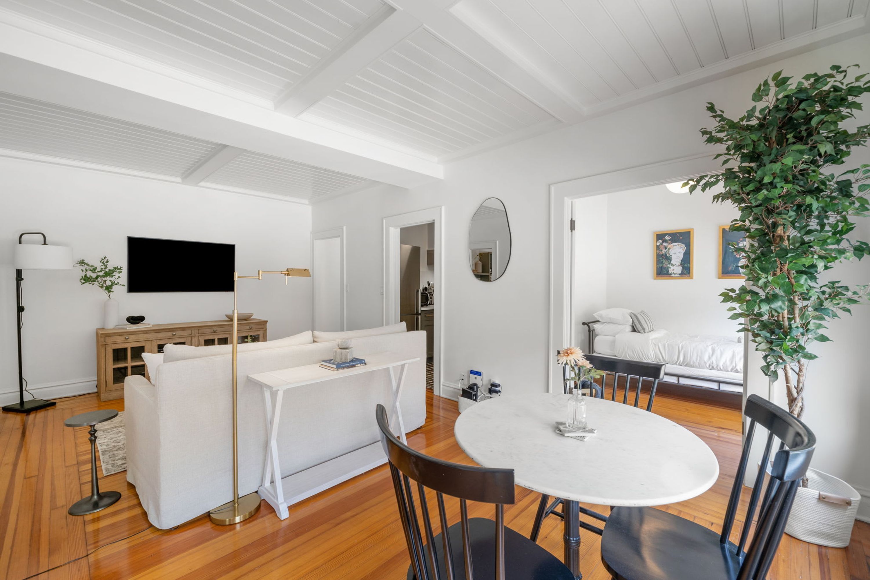 Un salon moderne avec un canapé blanc, une table à manger avec des chaises, un téléviseur et une grande plante.