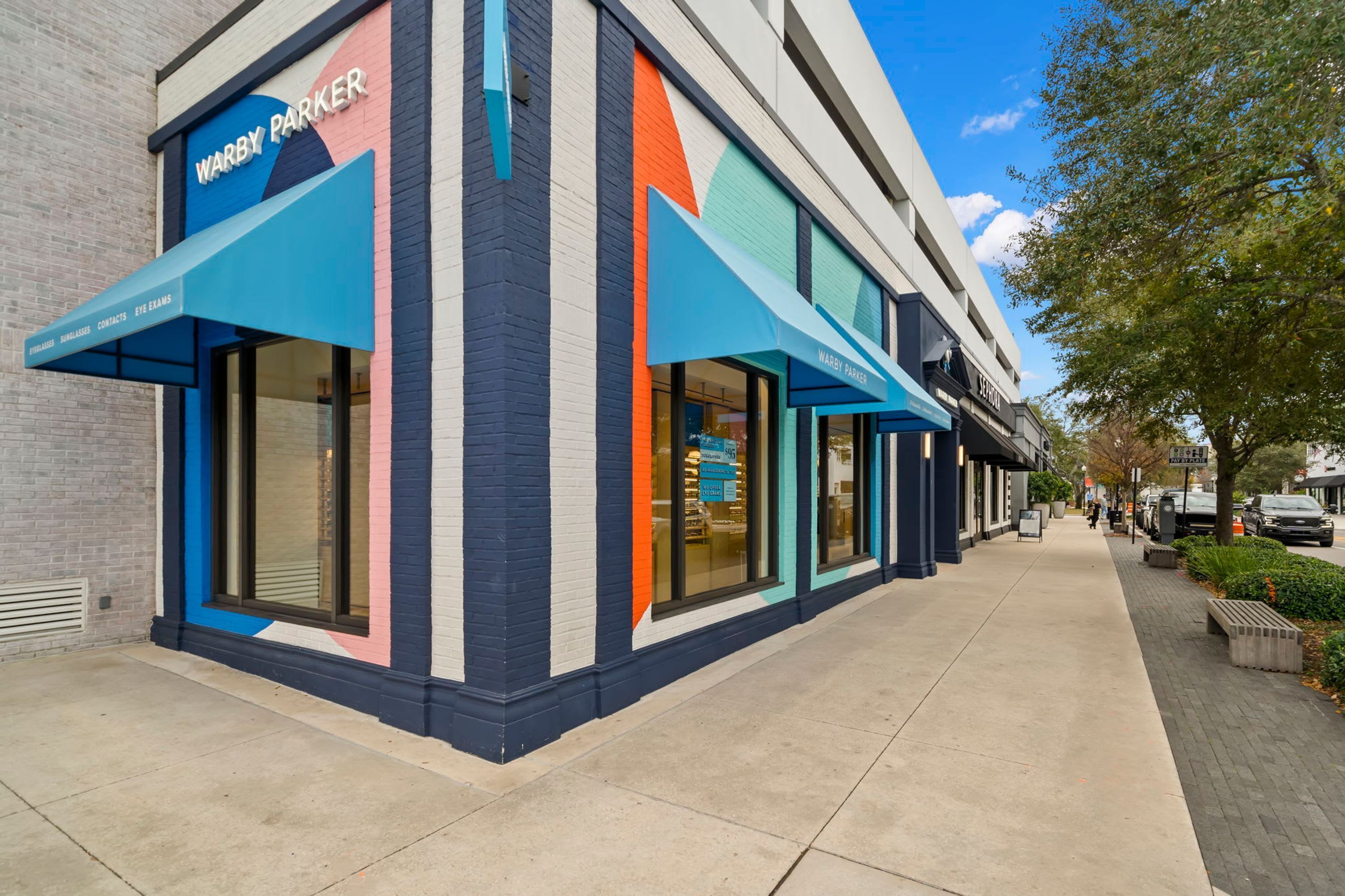 A modern building with a storefront labeled "Warby Parker" and a blue awning.