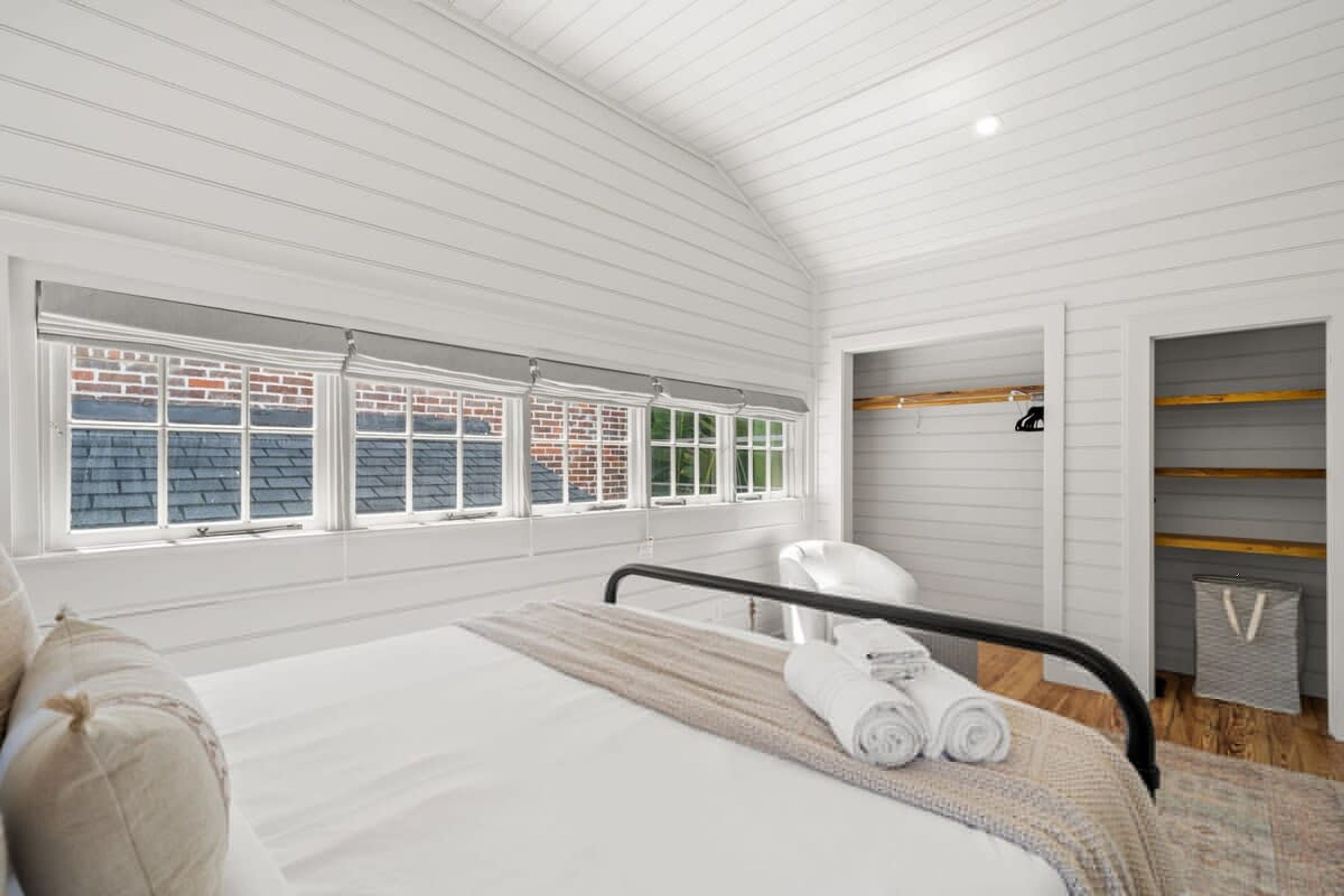 A bedroom with a bed, a window with a view of a brick building, a white ceiling, and a small closet with shelves.