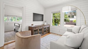 Un salón amplio con un sofá blanco, un mueble de madera y un televisor de pantalla plana montado en la pared.