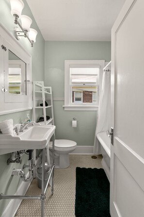 A compact bathroom with a white sink, a toilet, a window, and a shower area. - Soho Siesta Stunning Soho Apt w Private Balcony (Tampa)