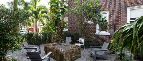 A courtyard with a stone fire pit, seating, and lush greenery.