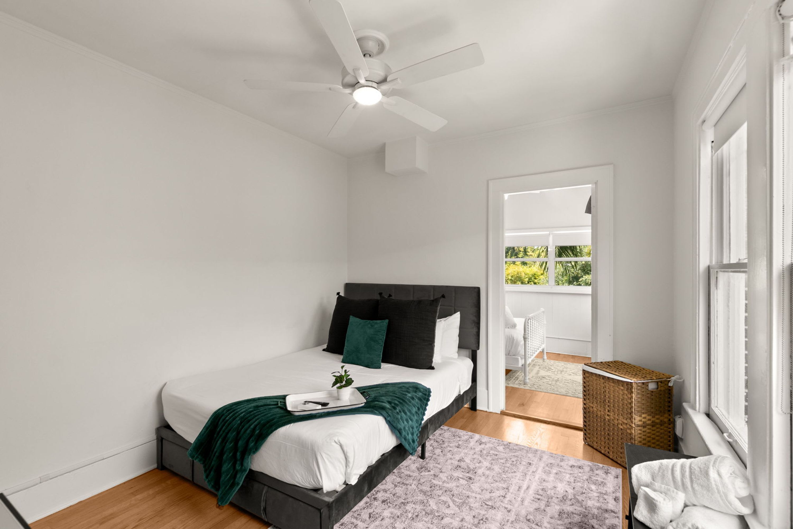Une chambre à coucher avec un lit, un ventilateur de plafond, une fenêtre et une vue sur la verdure à l’extérieur.