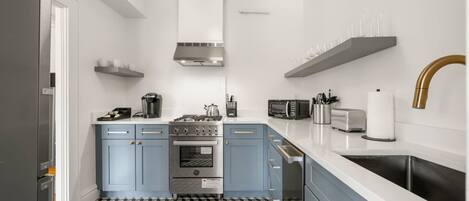 A compact kitchen with a central stove, microwave, and sink. There are cabinets with gold handles and a patterned floor.
