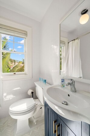 A bathroom with a toilet, sink, and mirror. There is a window with a view of greenery outside. - The Adaline 7 Luxury Hyde Park Apt (Tampa)