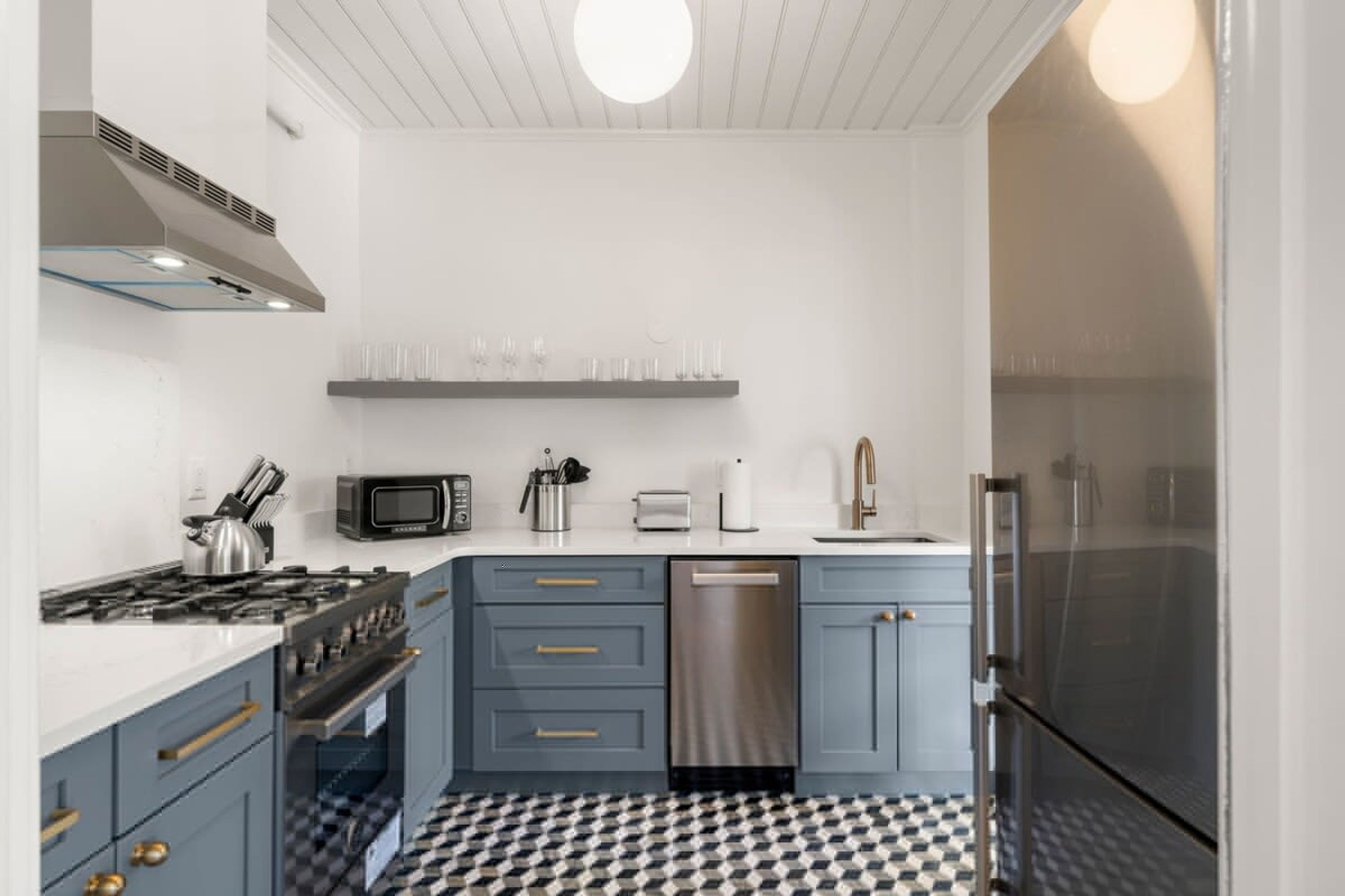 A modern kitchen with grey cabinets, stainless steel appliances, and a checkered floor.