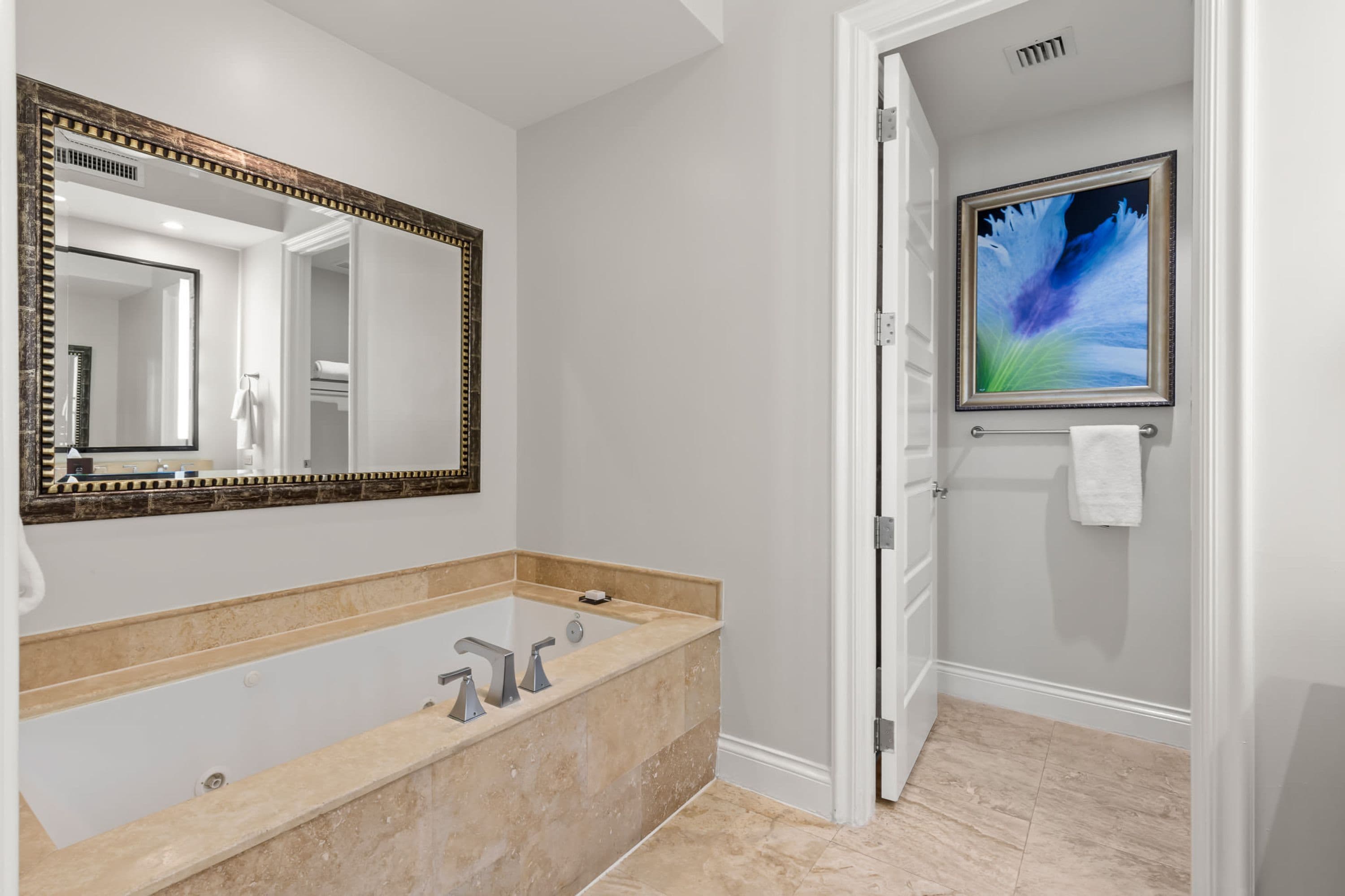 A bathroom with a large bathtub, a mirror, and a framed picture on the wall.