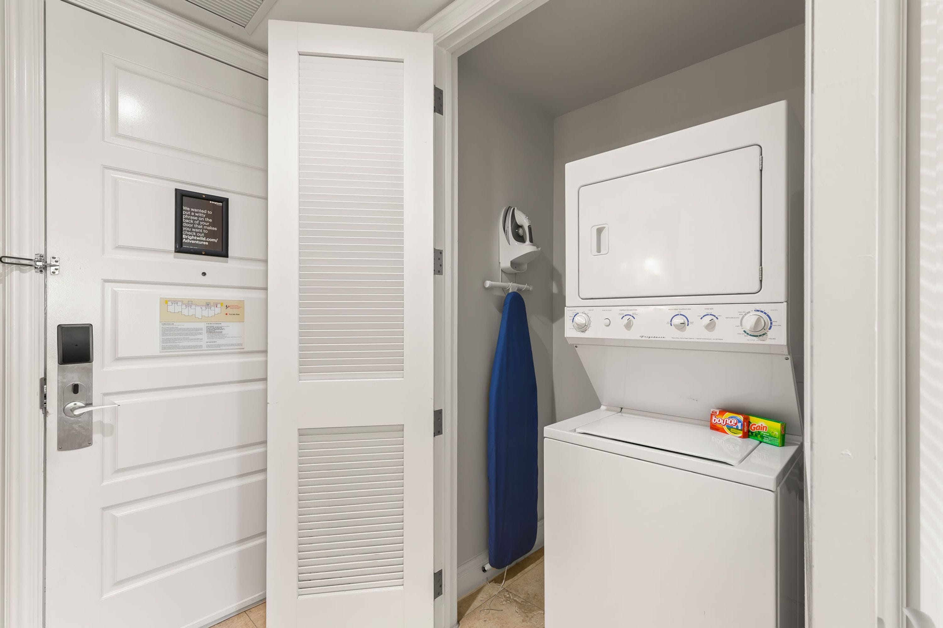 A laundry room with a white dryer, a wall-mounted iron, and a door with a sign.