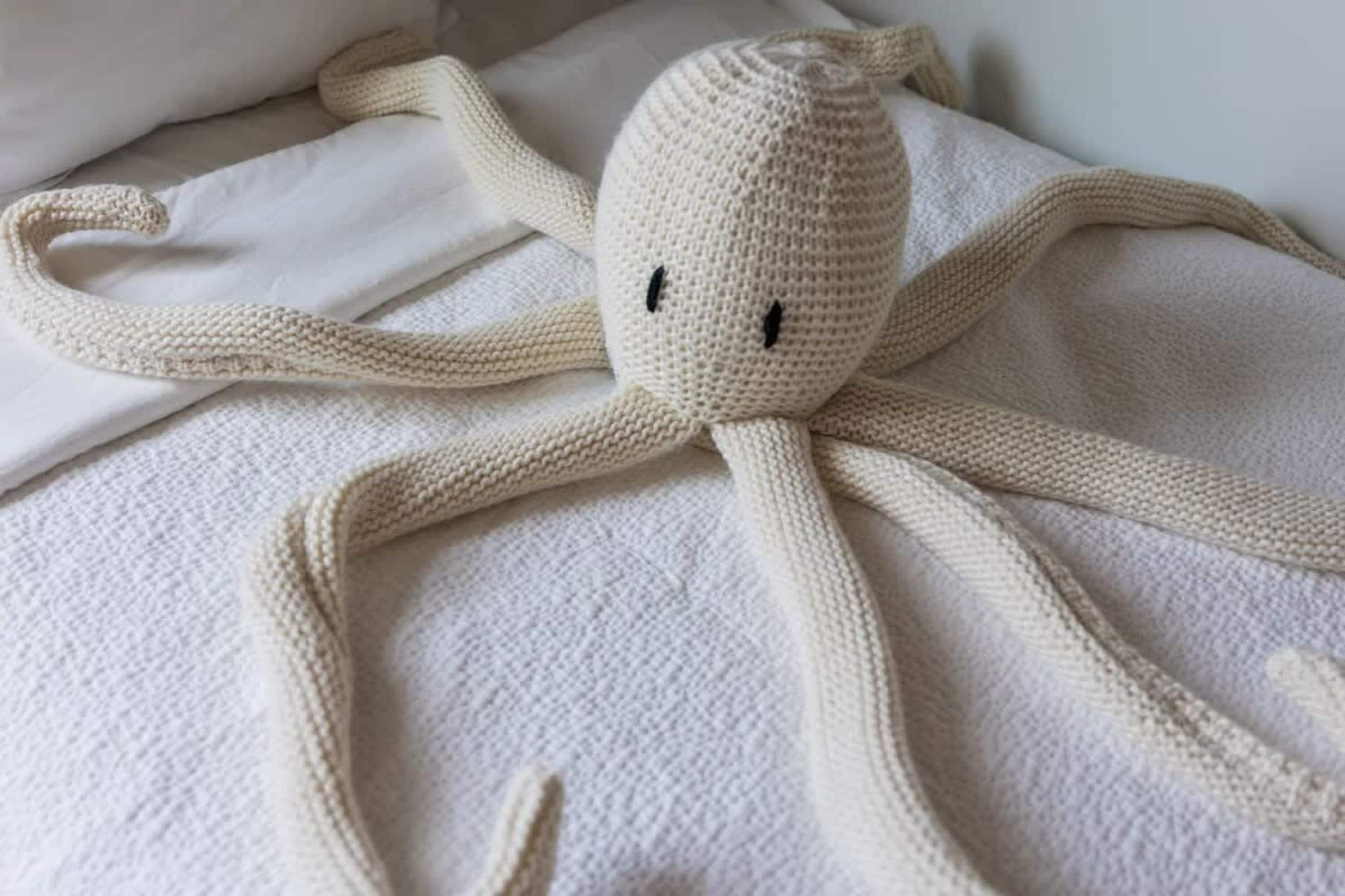 A knitted octopus toy on a white bedspread.