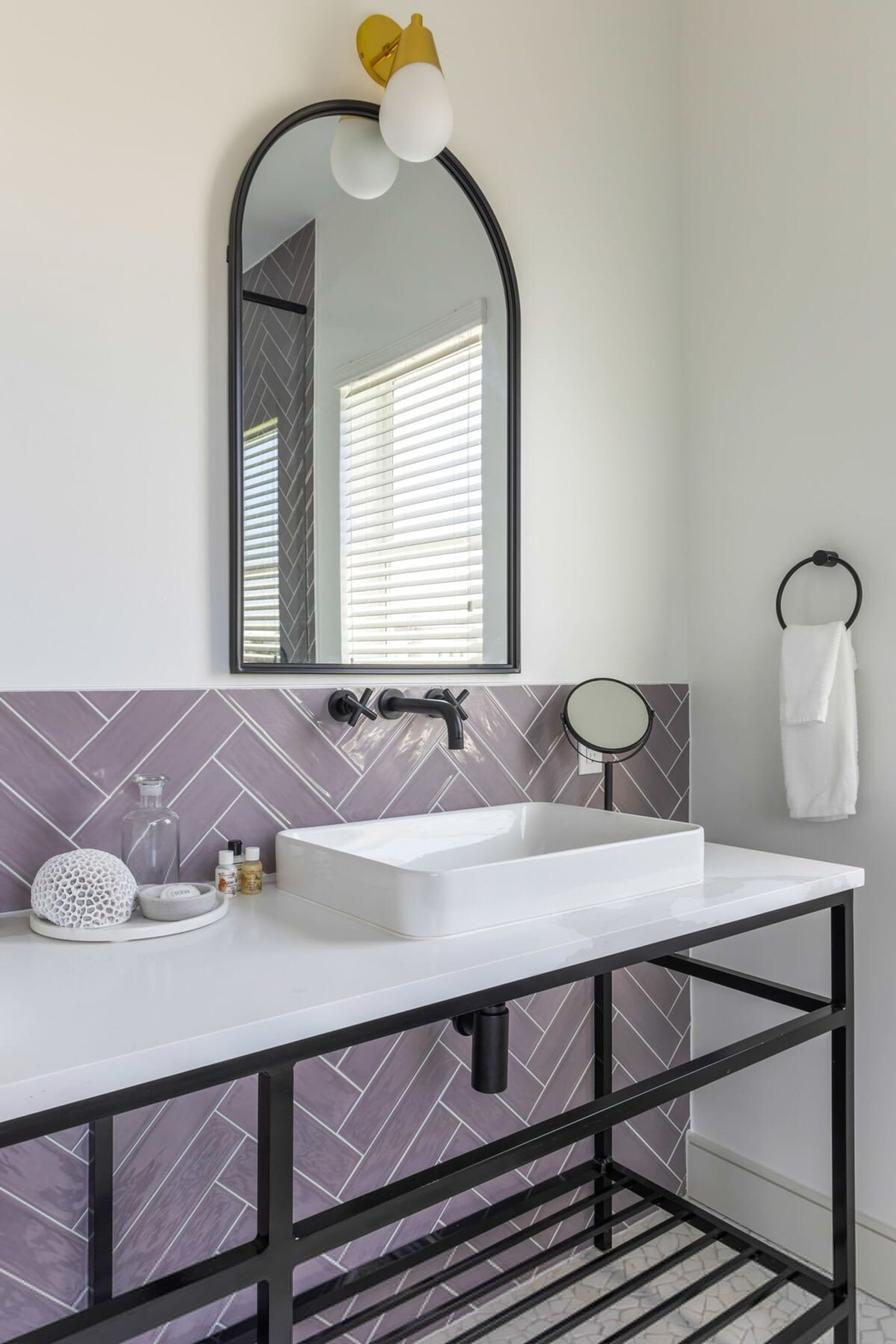 A bathroom with a white sink, black metal frame, and a mirror with a yellow light fixture.