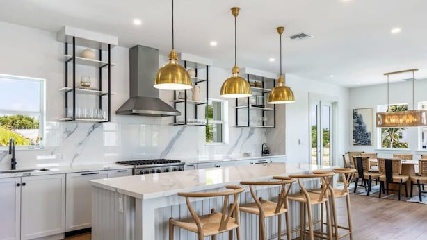 Una cocina moderna con armarios blancos, encimera de mármol y una isla central con taburetes de bar.