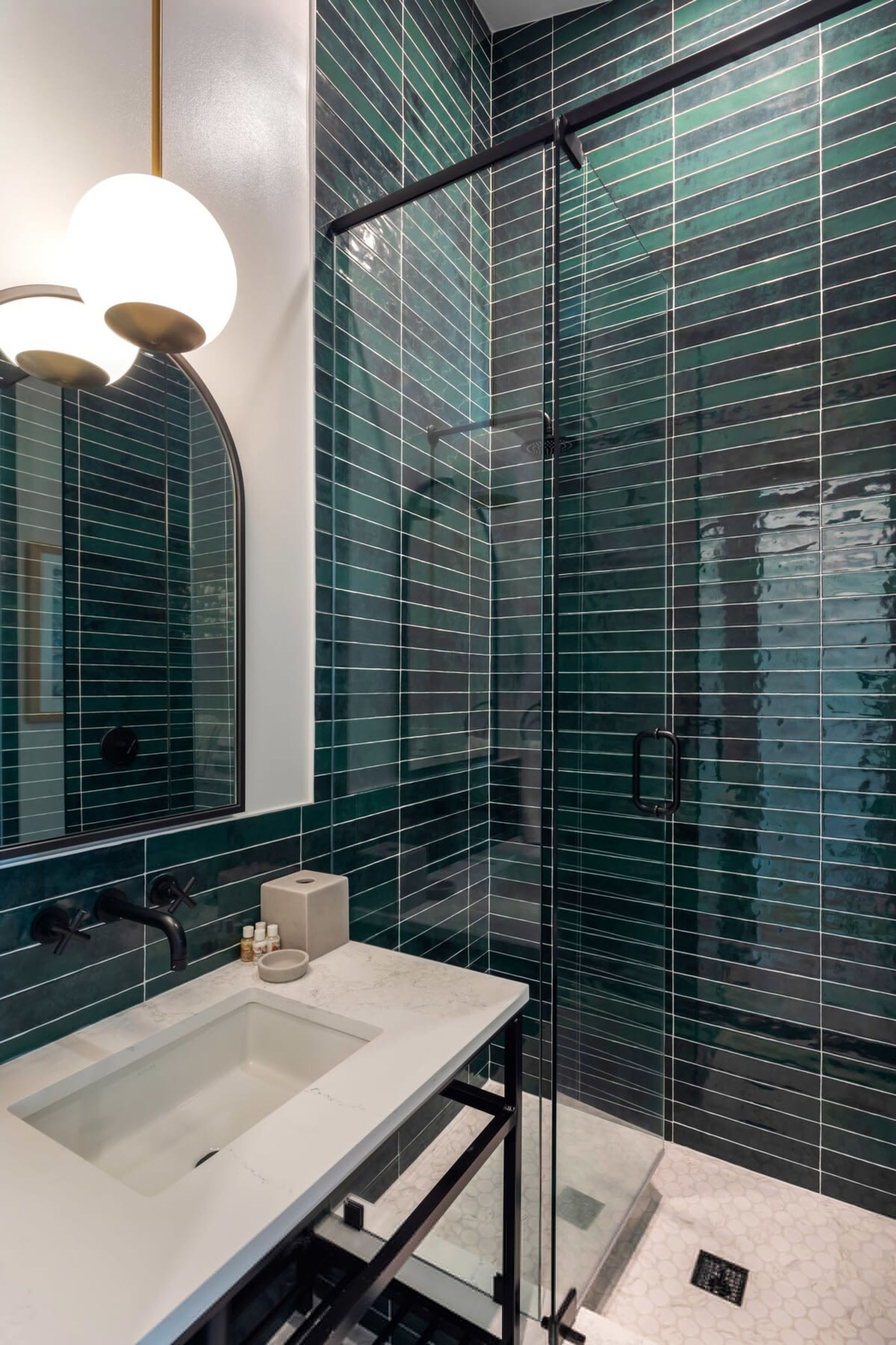 A modern bathroom with a glass shower enclosure, a large mirror, and a marble countertop.