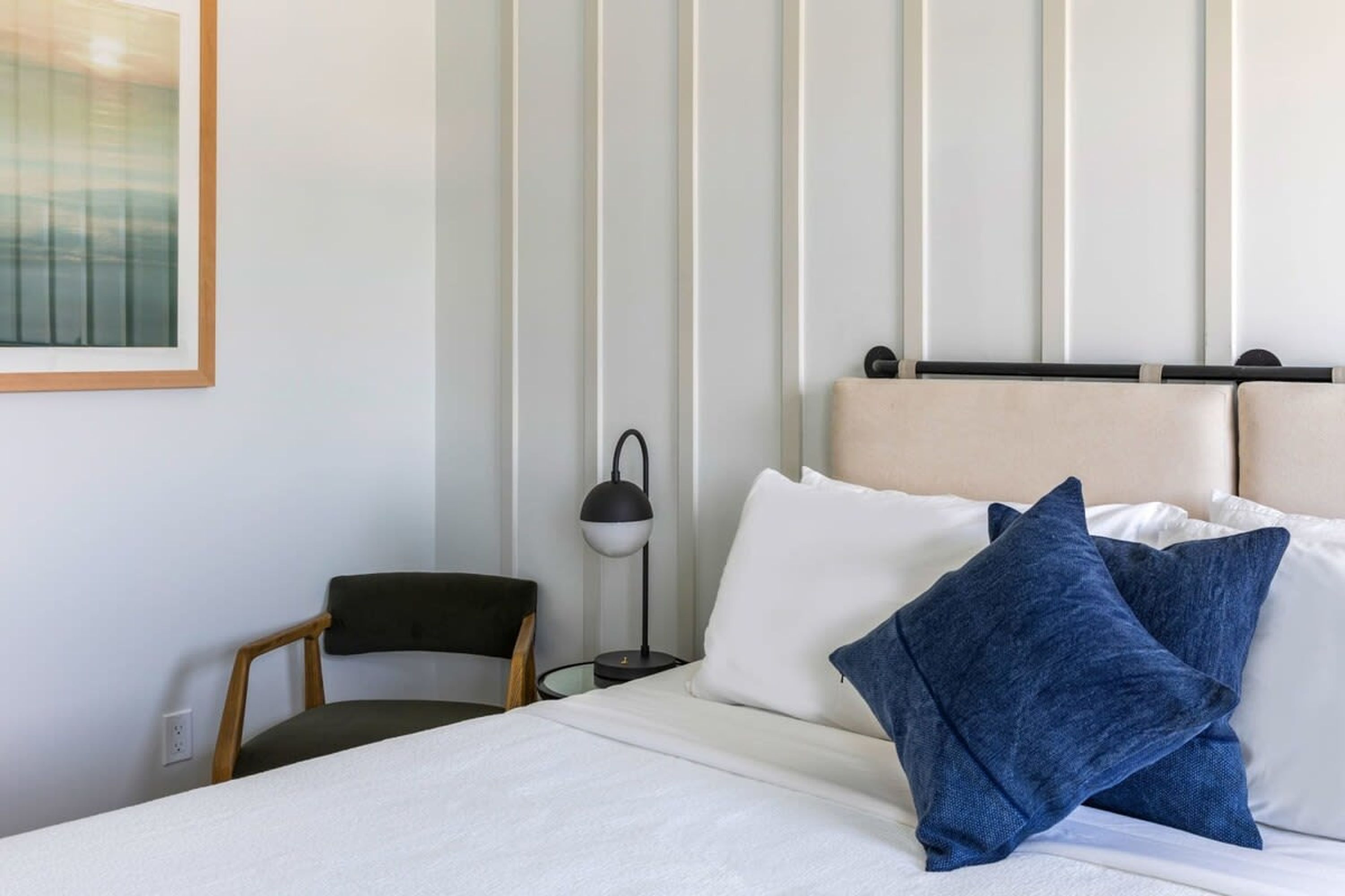A neatly arranged hotel room with a bed, pillows, a chair, and a bedside table with a lamp.