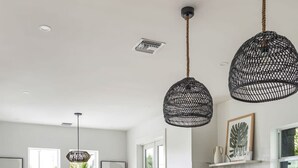 A modern kitchen with a central island, bar stools, pendant lights, and a view of the outdoors.