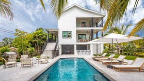 A two-story house with a swimming pool, outdoor seating, and a barbecue area.