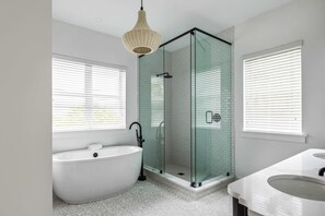 A modern bathroom with a freestanding bathtub, a glass-enclosed shower, and a vanity with two sinks. - New Windrose House by Brightwild Pool (Key West)