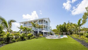 A two-story house with a pool, surrounded by a well-maintained lawn and palm trees.